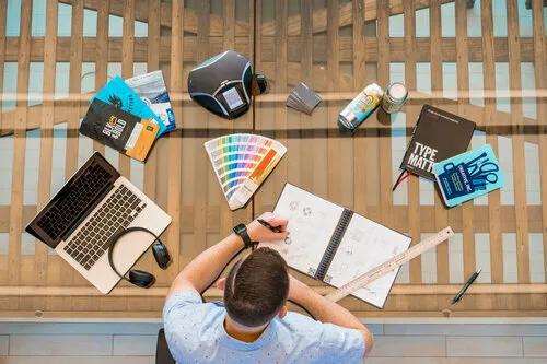 Overhead view of a designer at a desk with color swatches, laptop and camera