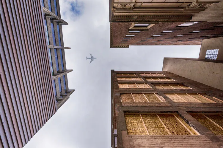 Looking straight up between two buildings at an airplane crossing the sky