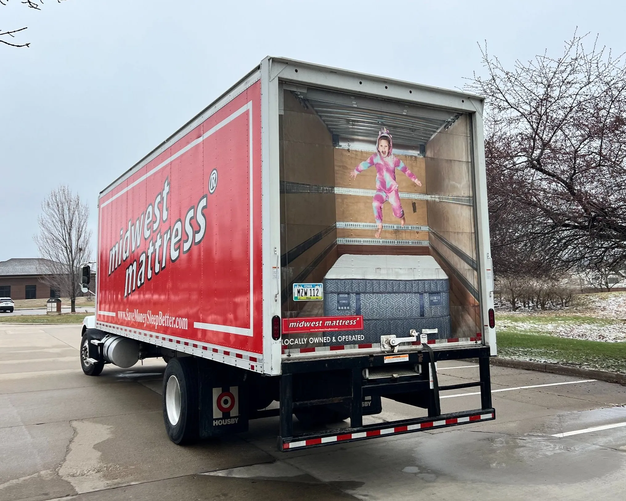 Red Midwest Mattress delivery truck on a wet street in spring