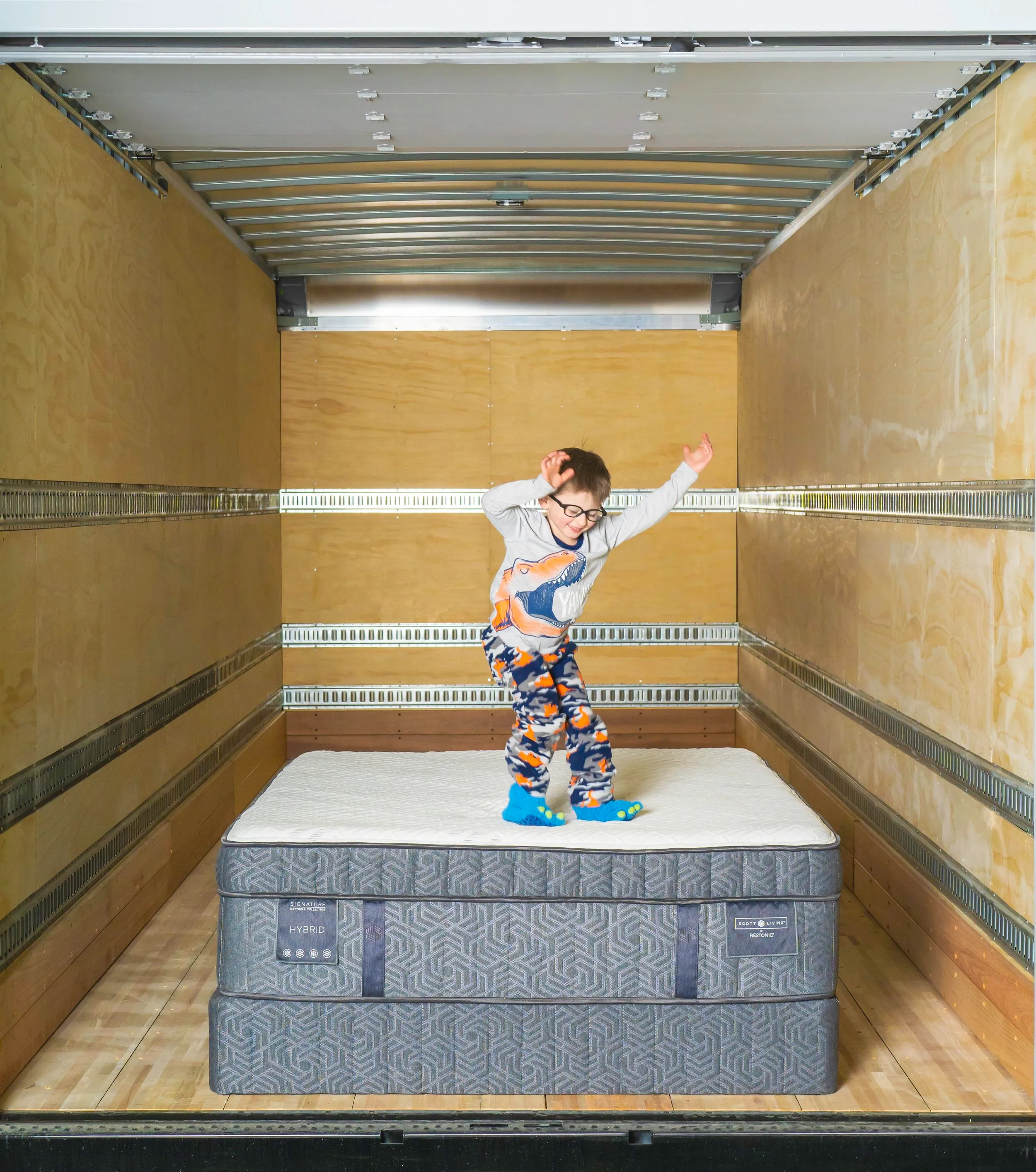 Child jumping on a mattress in the back of a Midwest Mattress delivery truck